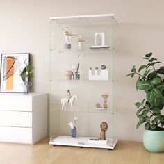 a glass shelf with figurines on it next to a potted plant