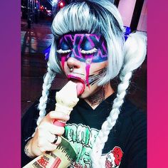 a woman with white hair and face paint eating an ice cream cone