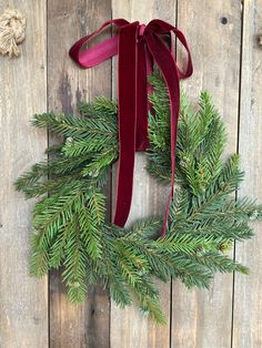 a christmas wreath with red ribbon hanging on a wooden wall next to a pair of scissors