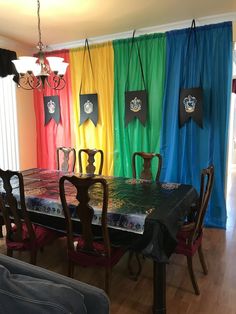 a dining room table with colorful curtains on the wall behind it and chairs around it