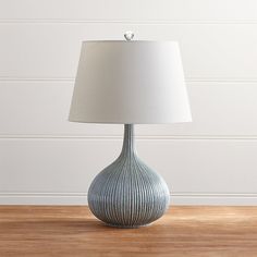 a lamp on a wooden table in front of a white wall and wood flooring