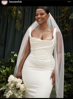 a woman in a white dress and veil posing for the camera with her wedding bouquet