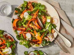 two plates filled with salad on top of a table next to silverware and utensils