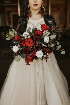 a woman in a wedding dress holding a bouquet of red and white flowers on her shoulder