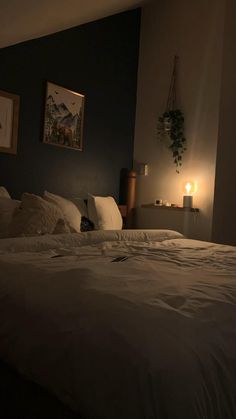 a bed with white sheets and pillows in a dark room next to a lit candle