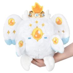 a hand holding a white stuffed animal with gold accents