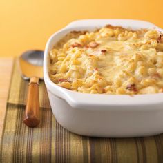 a casserole dish with cheese and meat in it next to a wooden spoon