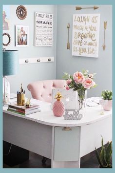 a white desk topped with lots of pink flowers next to a lamp and pictures on the wall