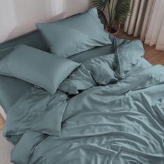 an unmade bed with blue sheets and pillows on the floor next to a potted plant