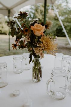 a vase filled with flowers sitting on top of a white table covered in glass jars