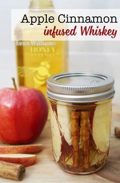 an apple cinnamon infused whiskey in a glass jar next to apples and cinnamon sticks on a cutting board