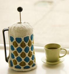 a knitted tea cosy next to a cup of coffee on a window sill