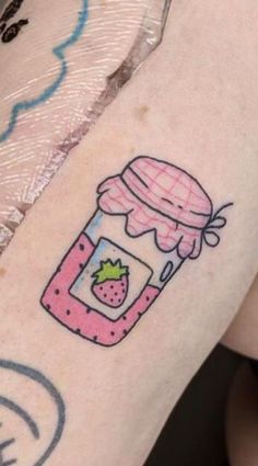 a woman's arm with a jar of strawberry jam tattooed on the back of it