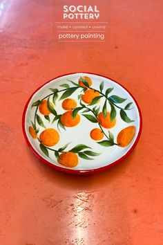 a plate with oranges painted on it sitting on a red countertop next to the words social pottery