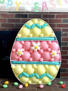 an egg shaped cake sitting in front of a fireplace with balloons and candies around it