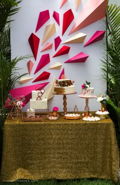 a table topped with cakes and desserts next to a wall covered in paper art