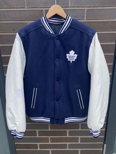 Vintage 1990s Toronto Maple Leafs Reversible Jacket - No Tag (Length 25" Chest 20") - Fits: Medium - Overall used vintage condition - Hole on left arm varsity side - Staining on collar/right shoulder (see pictures) - Message for more information Please take note of the measurements listed as these are vintage clothes and may fit different than the tag size. Follow our page for more vintage clothing drops! DISCLAIMER: All items are vintage so please be mindful that if by chance there is a flaw on Retro Winter Outerwear With Embroidered Graphics, Varsity Outerwear With Embroidered Baseball Collar, Casual White Outerwear With Embroidered Patch, White Embroidered Crew Neck Outerwear, White Embroidered Outerwear For College, White Varsity Outerwear With Embroidered Graphics, White Embroidered Patch Long Sleeve Outerwear, White Long Sleeve Outerwear With Embroidered Patch, Collegiate Long Sleeve Outerwear With Embroidered Patch