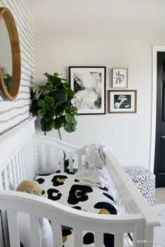 a white crib with black and white bedding, pictures on the wall and a potted plant