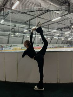 a woman standing on one leg while doing a handstand in front of an ice rink