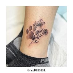 a black and white photo of a flower tattoo on the ankle, with paw prints