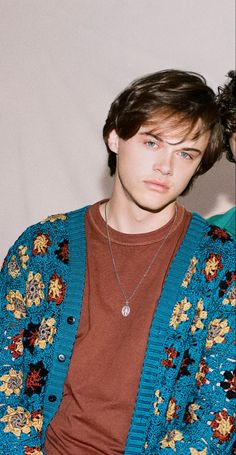 a young man wearing a blue cardigan and brown t - shirt