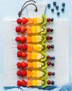 fruit skewers are arranged on a cutting board with berries and kiwis