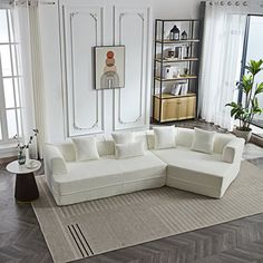 a large white sectional couch in a living room with wood flooring and open windows