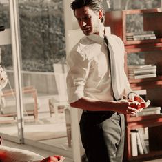 a man in a white shirt and tie standing next to a book shelf filled with books