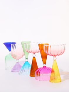 four different colored wine glasses sitting next to each other on a white surface with no one around them