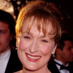 a woman in a red dress smiling at the camera with other people behind her looking on