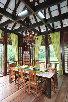 a dining room with wooden floors and green drapes on the windows, along with a table surrounded by chairs