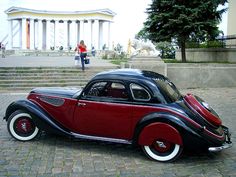 an antique car parked on the side of a road in front of a building with columns