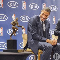 two men in suits sitting next to each other at a press conference with basketball statues behind them