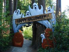 there is a sign that says happy halloween with ghost heads on it in the woods