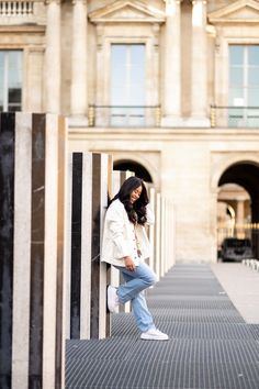 a woman leaning against a wall in front of a large building with columns and pillars