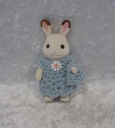 a small stuffed animal with a blue dress on it's chest and ears is standing in front of a white background