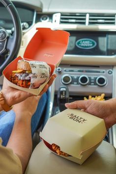 two people sitting in the driver's seat of a car eating food from boxes