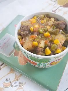 a white bowl filled with stew on top of a green place mat next to a book