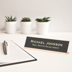 a notepad and pen sitting on top of a desk next to two potted plants