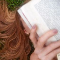 a woman laying on the ground reading a book with her eyes closed and hair blowing in the wind