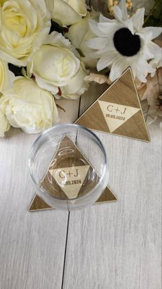 two small triangle shaped tags sitting on top of a wooden table next to white flowers