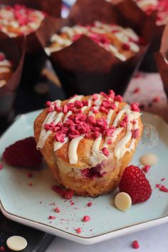 some cupcakes with white frosting and raspberries on a plate