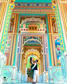 two people standing in front of a colorful building with ornate decorations on the walls and doors