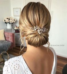 a woman with her hair in a low updo and some flowers on the side