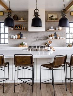 a kitchen with three black pendant lights hanging over the counter and four brown chairs in front of it