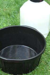 a black bowl sitting on the grass next to a bottle of milk and a jug