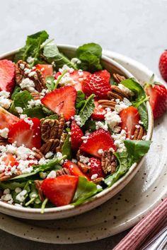 a salad with strawberries, pecans and feta cheese in a white bowl