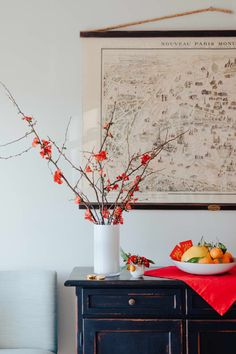 a bowl of fruit is sitting on a table next to a vase with flowers in it