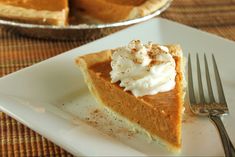 a slice of pumpkin pie on a white plate with a fork next to the pie