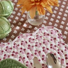 an orange flower is in a glass vase on a table with plates and spoons